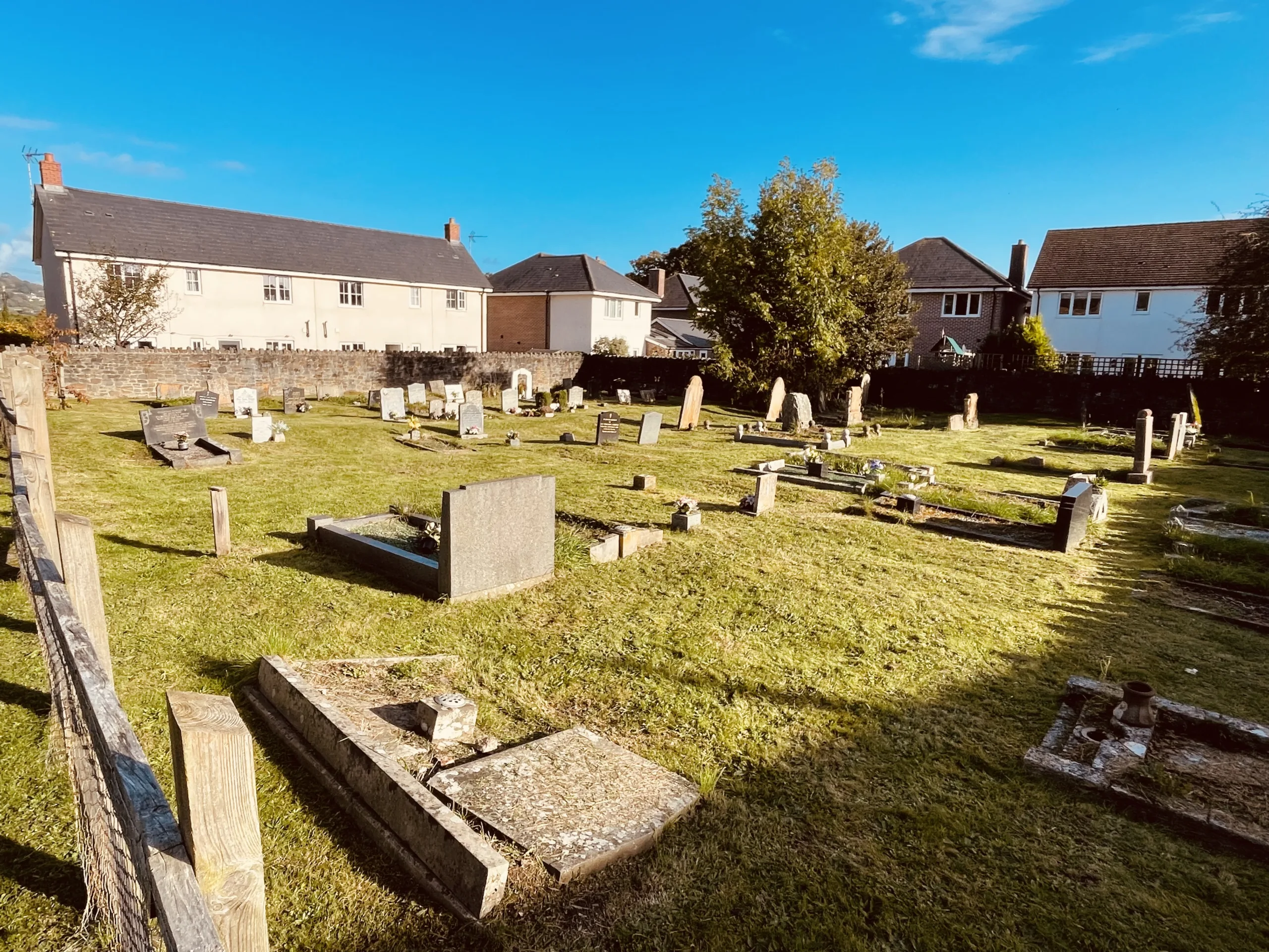Row upon row of weathered headstones and stone kerbs in the chapel graveyard, with the rebuilt stone wall and village rooftops beyond